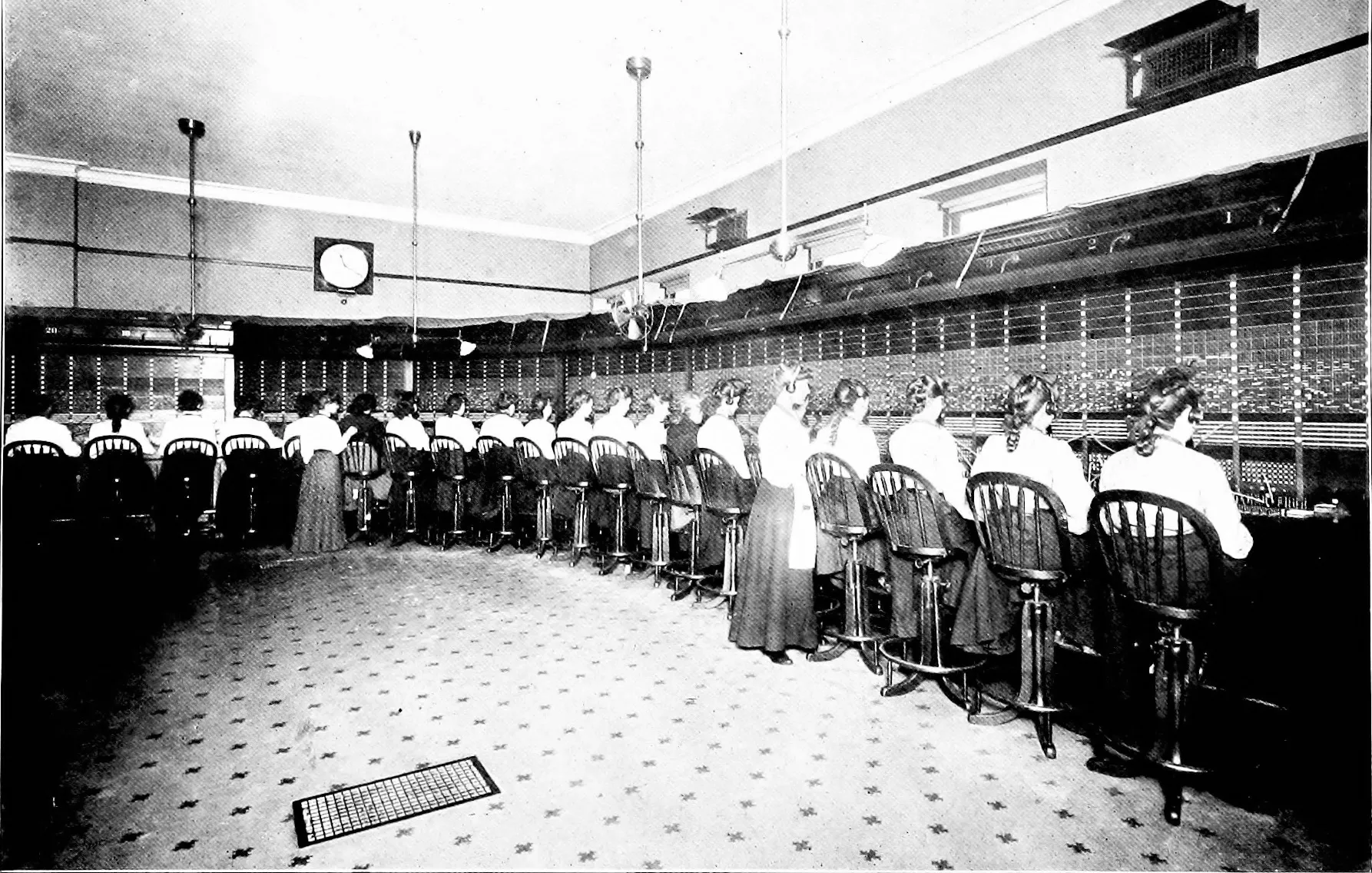 A long telephone switchboard with a row of operators seated at it.